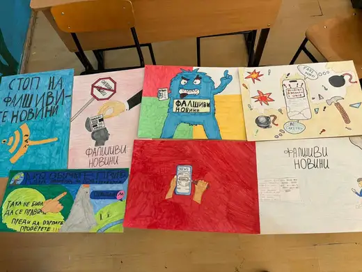 Четири нарисувани плаката за фалшивите новини, подредени на маса.