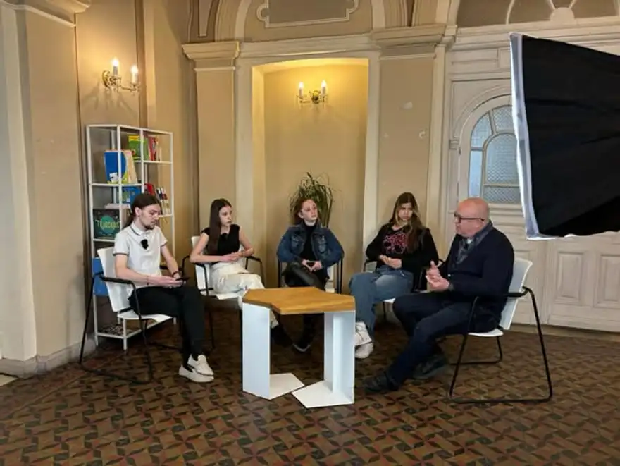 Четирима ученици и мъж седят около ниска маса в зала на центъра.