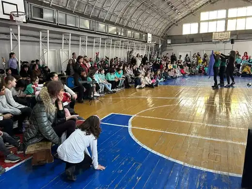 Деца седят по пода на салона и гледат представление.