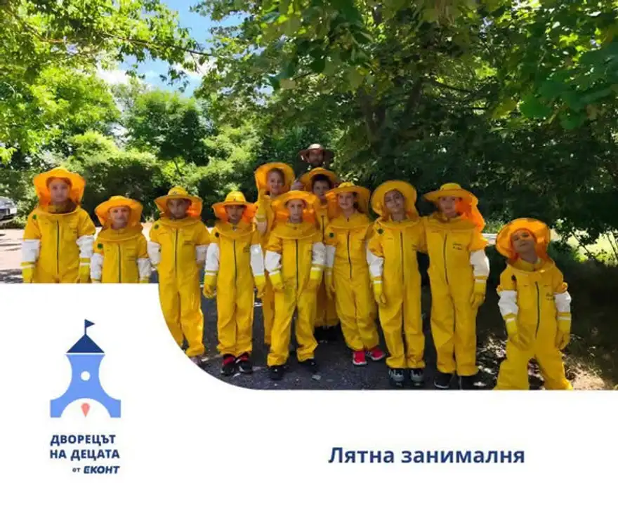 Деца в жълти пчеларски костюми със защитни шапки стоят под голямо зелено дърво край горски път.